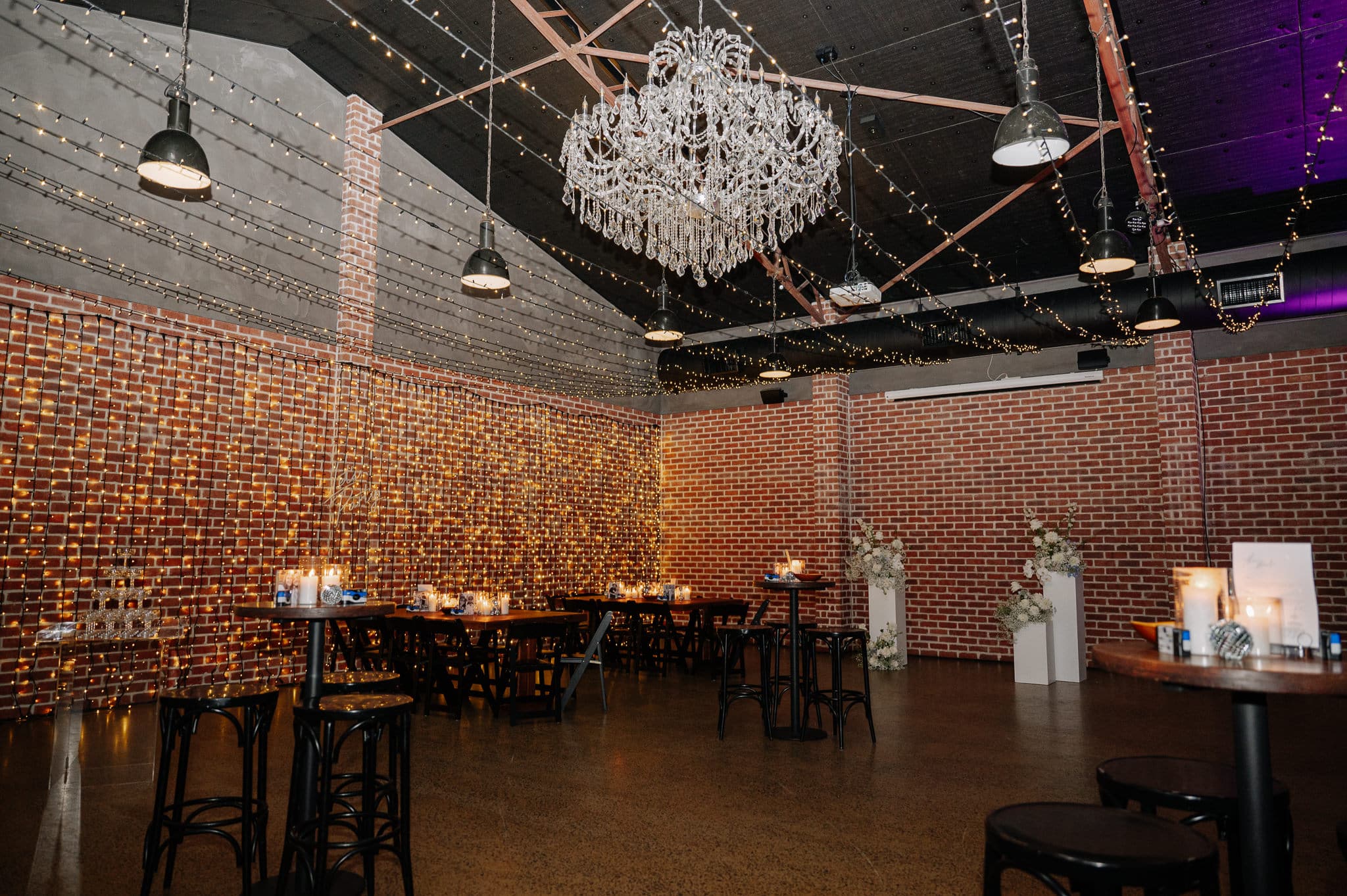 Rustic-industrial function room at Factory 51 set up for an engagement party in Brisbane, featuring fairy lights, chandelier, and elegant table styling.
